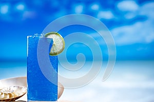 Blue slush ice in glass on sea beach background