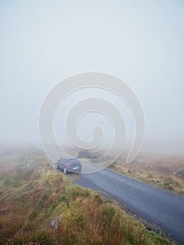 Blue small car parked on a small narrow country road during fog. Dangerous driving conditions due to poor visibility. Nature scene