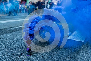 A blue smoke bomb is seen among protesters marching during a protest in the street with people uprising