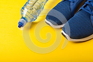 Blue sneakers and bottle of water on yellow background. Concept of healthy lifestile, everyday training and force of will