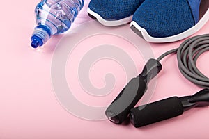 Blue sneakers, skipping rope and bottle of water on pink background. Concept of healthy lifestile, everyday training and force of