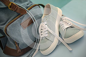 Blue sneakers with white laces and backpack on a light blue background.