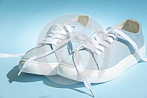 Blue sneakers with white laces on a light blue background.