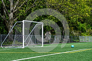 Blue soccer ball on an artificial turf field and white netted goal on a sunny spring day