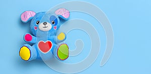 Blue soft children`s toy puppy with funny ears, multi-colored paws and red heart on blue background flat lay top view