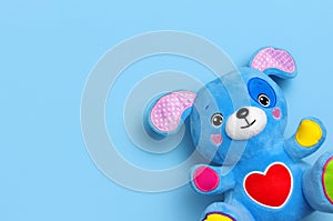 Blue soft children`s toy puppy with funny ears, multi-colored paws and red heart on blue background flat lay top view