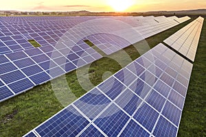 Blue solar photo voltaic panels system producing renewable clean energy on rural landscape and setting sun background