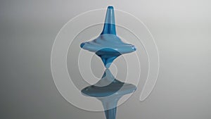 Blue spinning top spinning. Whirligig in action is reflected on mirror surface. Slow motion