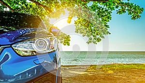 Blue sport SUV car parked by the tropical sea under umbrella tree. Summer vacation at the beach. Summer travel by car. Road trip.