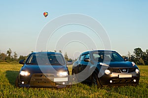 Blue sports car in a field and aerostat balloon at background
