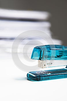Blue stapler on table with stack of papers in background