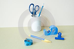 Blue stationery. Colored pencil, pen, scissors, clip, tape measure, tape dispenser on desk. white ivory background