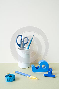 Blue stationery. Colored pencil, pen, scissors, clip, tape measure, tape dispenser on desk. white ivory background