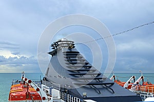 Blue steamer pipe with light brown smoke. Lifeboat on deck of a cruise ship. Sea and blue sky with clouds in the background.