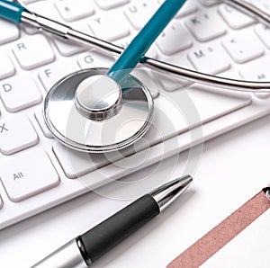 Blue stethoscope on computer keyboard on white table background. Online medical information treatment technology concept, close up