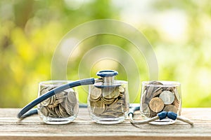 Blue stethoscope and jar of coin on wooden table. Money and financial checking concept
