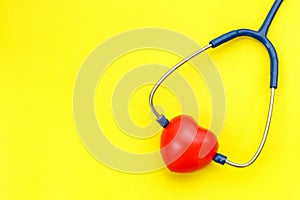 Blue stethoscope and red heart shape on yellow background. For c