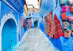 Blue street of Chefchaouen in Morocco with colorful carpets and handicrafts on walls