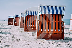 Blue striped roofed wooden chairs stands in line on sandy beach on sunny day. Travemunde, Luebeck, Germany