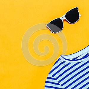blue striped t-shirt and white sunglasses on bright yellow background, summer time. Top view, flat lay, minimalism