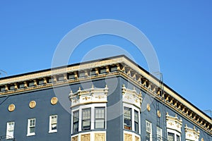 Blue stucco building with golden decorative facade with white accent paint around windows with flat roof and blue sky