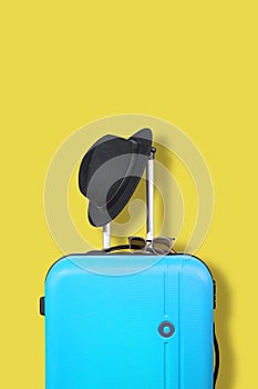 Blue suitcase and black hat on a yellow background