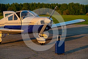 A blue suitcase and a landed small private jet. Four-seater plane with a propeller for the air taxi. Self travel concept