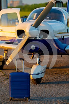 A blue suitcase and a landed small private jet. Four-seater plane with a propeller for the air taxi. Self travel concept
