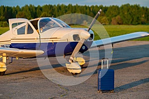 A blue suitcase and a landed small private jet. Four-seater plane with a propeller for the air taxi. Self travel concept