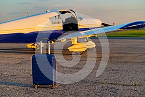 A blue suitcase and a landed small private jet. Four-seater plane with a propeller for the air taxi. Self travel concept