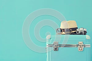 Blue suitcase with sun glasses, hat and camera on pastel blue background.