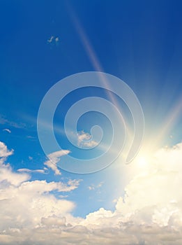 Blue summer sky with fluffy clouds and bright sun as a background. Vertical photo