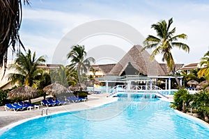 Blue sunbeds under thatch-covered sunshades stand near a swimming pool