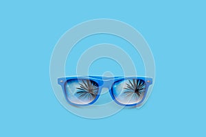 Blue sunglasses with palm tree reflections isolated in a large pastel blue background. Minimal image concept for ready for summer