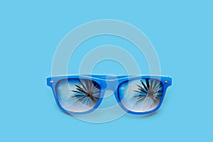 Blue sunglasses with palm tree reflections isolated in pastel blue background. Minimal image concept for ready for summer, sun