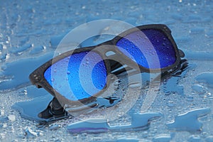 Blue sunglasses with water drops on water reflection