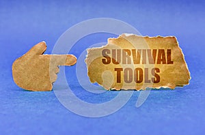 On a blue surface, a cardboard hand points to a sign with the inscription - Survival Tools