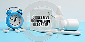 On a blue surface lie pills, an alarm clock and a notebook with the inscription - Obsessive Compulsive Disorder