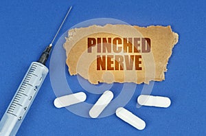 On a blue surface lie a syringe, pills and a cardboard sign with the inscription - Pinched nerve