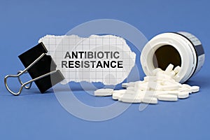 On the blue surface lies a jar of pills and a clip with paper on which is written - ANTIBIOTIC RESISTANCE