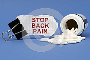 On the blue surface lies a jar of pills and a clip with paper on which is written - STOP BACK PAIN