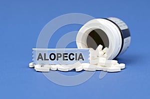 On a blue surface lies a jar of pills and a sign with the inscription - ALOPECIA