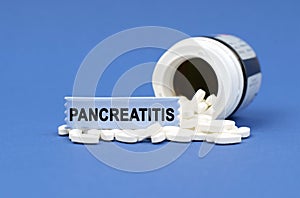On a blue surface lies a jar of pills and a sign with the inscription - PANCREATITIS