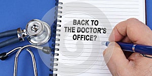 On a blue surface lies a stethoscope and a notebook in which it is written by hand - Back to the doctor& x27;s office