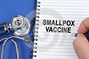 On a blue surface lies a stethoscope and a notebook in which it is written by hand - smallpox vaccine