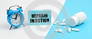 On a blue surface are pills, on a white surface an alarm clock and a plate with the inscription - Heparin Injection