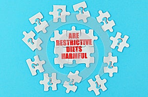 On a blue surface are puzzles with a question mark, in the center with the inscription - Are restrictive diets harmful