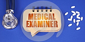 On the blue surface of the tablet, a stethoscope and a notepad with the inscription - MEDICAL EXAMINER