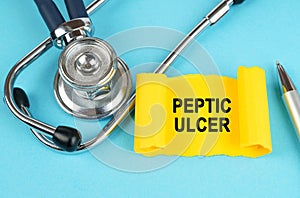 On the blue surface there is a stethoscope, a pen and a yellow sticker with the inscription - Peptic ulcer