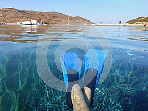 Blue swimfins on female legs in crystal clear water of Kolona double bay Kythnos island Cyclades Greece, Aegean sea.